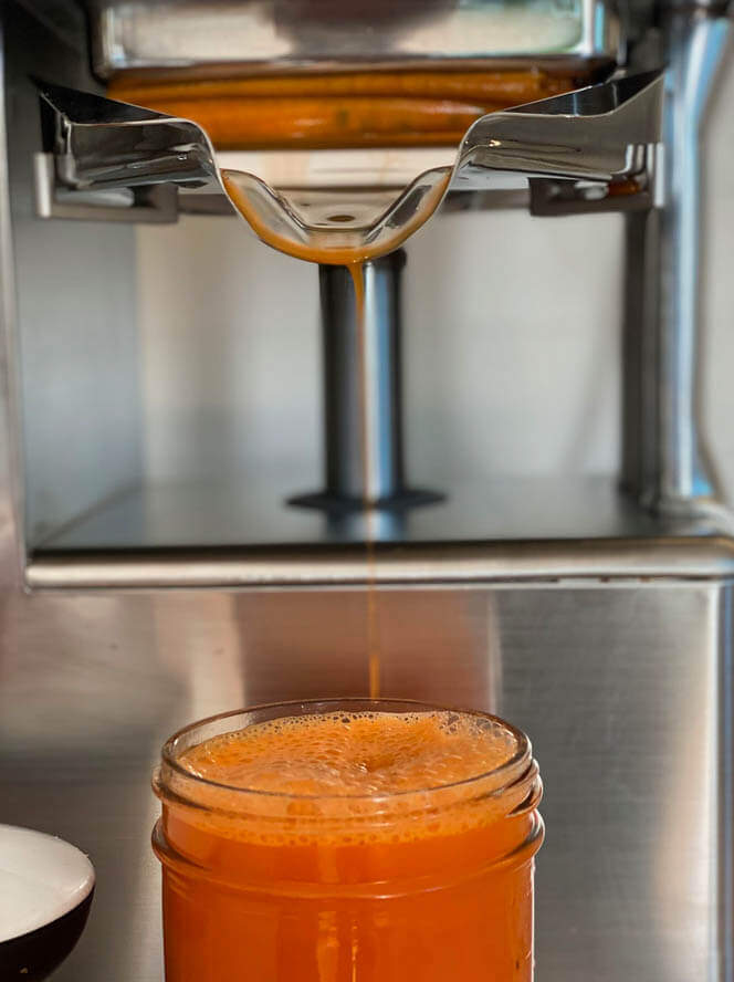 orange colored juice coming from juicer
