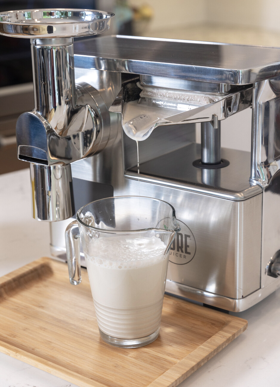 Fresh homemade almond milk in a glass measuring cup positioned under the PURE Juicer press.