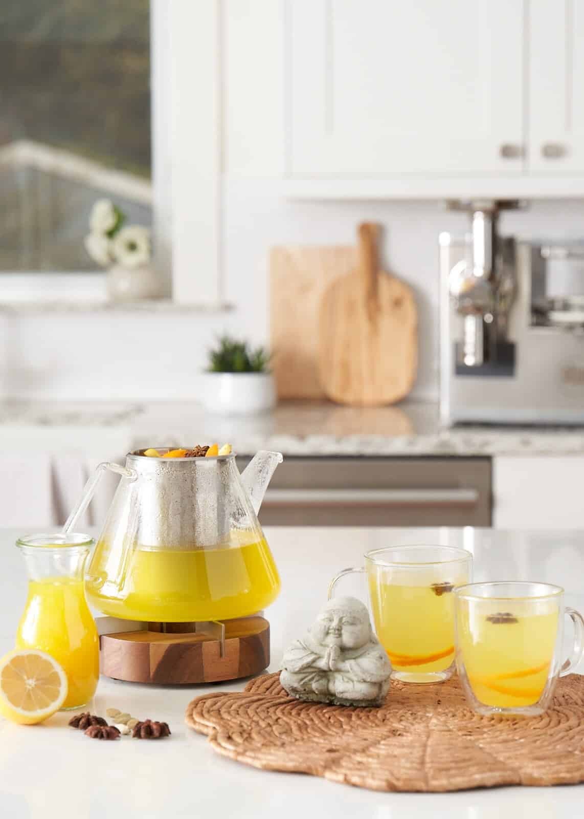 tea kettle and glass teacups filled with bright yellow tea made from juice pulp