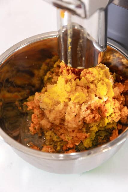 Sweet potato juice ingredients, ground, in a stainless steel bowl below a PURE Juicer grinder.