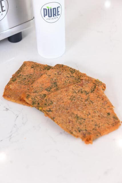 Orange and green sweet potato pulp, laid out in a fan formation in front of a white PURE Juicer thermos.