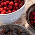 A bowl of black grapes sits in front of two bowls full of fresh cranberries.