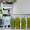 Five bottles of green juice are lined up on a kitchen counter, next to a PURE Juicer.