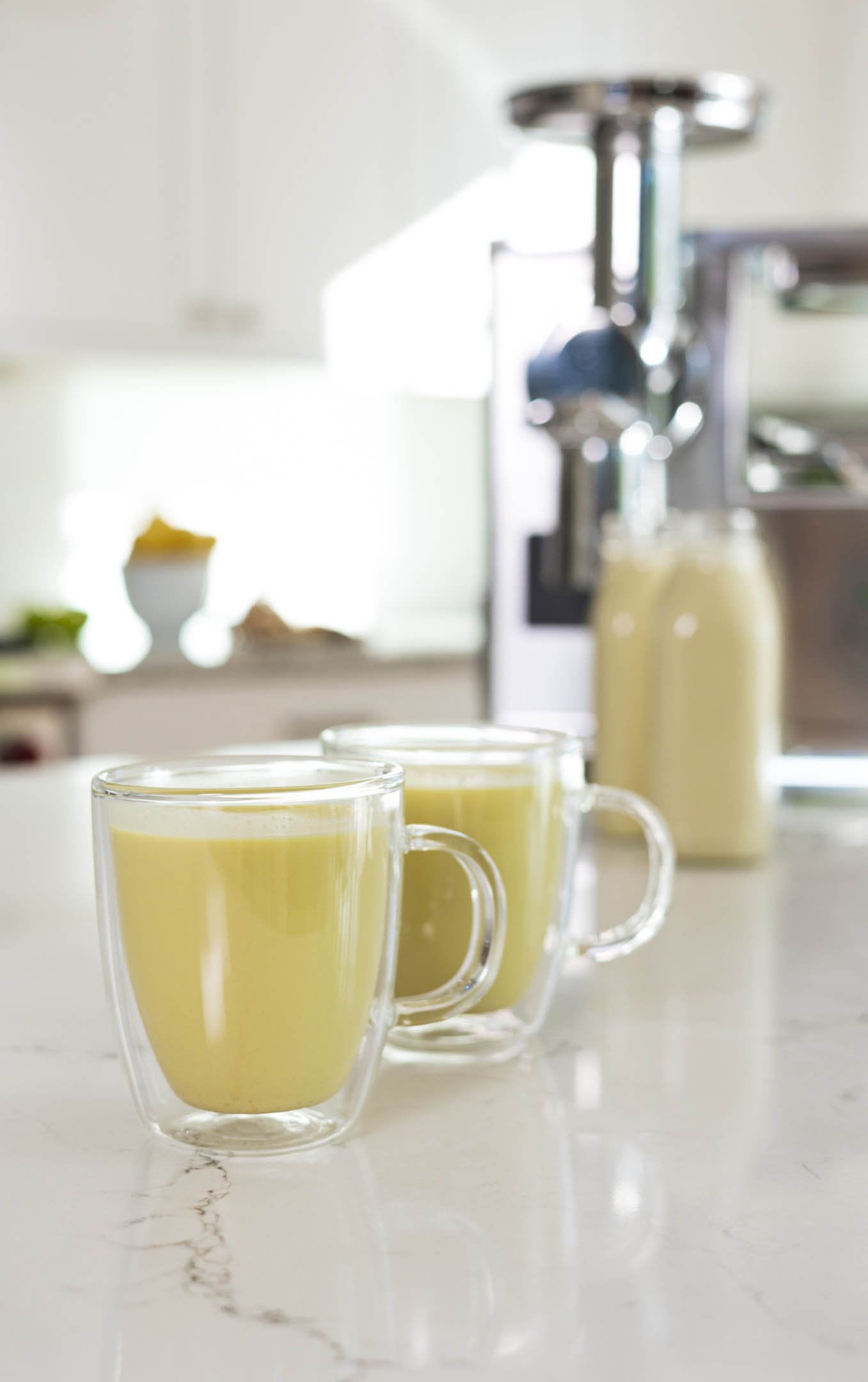 soothing turmeric milk recipe with homemade almond milk and pressed turmeric, ginger, cardamom, and cinnamon juice in cups