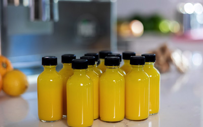 Glass bottles holding immune-boosting ginger turmeric orange lemon wellness shots sit together on a countertop in front of a PURE Juicer.