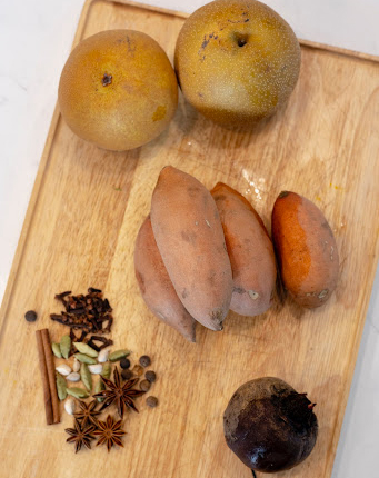 Ingredients for sweet potato-asian-pear spice juice rest on a cutting board: asian pears, sweet potatoes, cinnamon, cardamon, star anise, and black peppercorn.