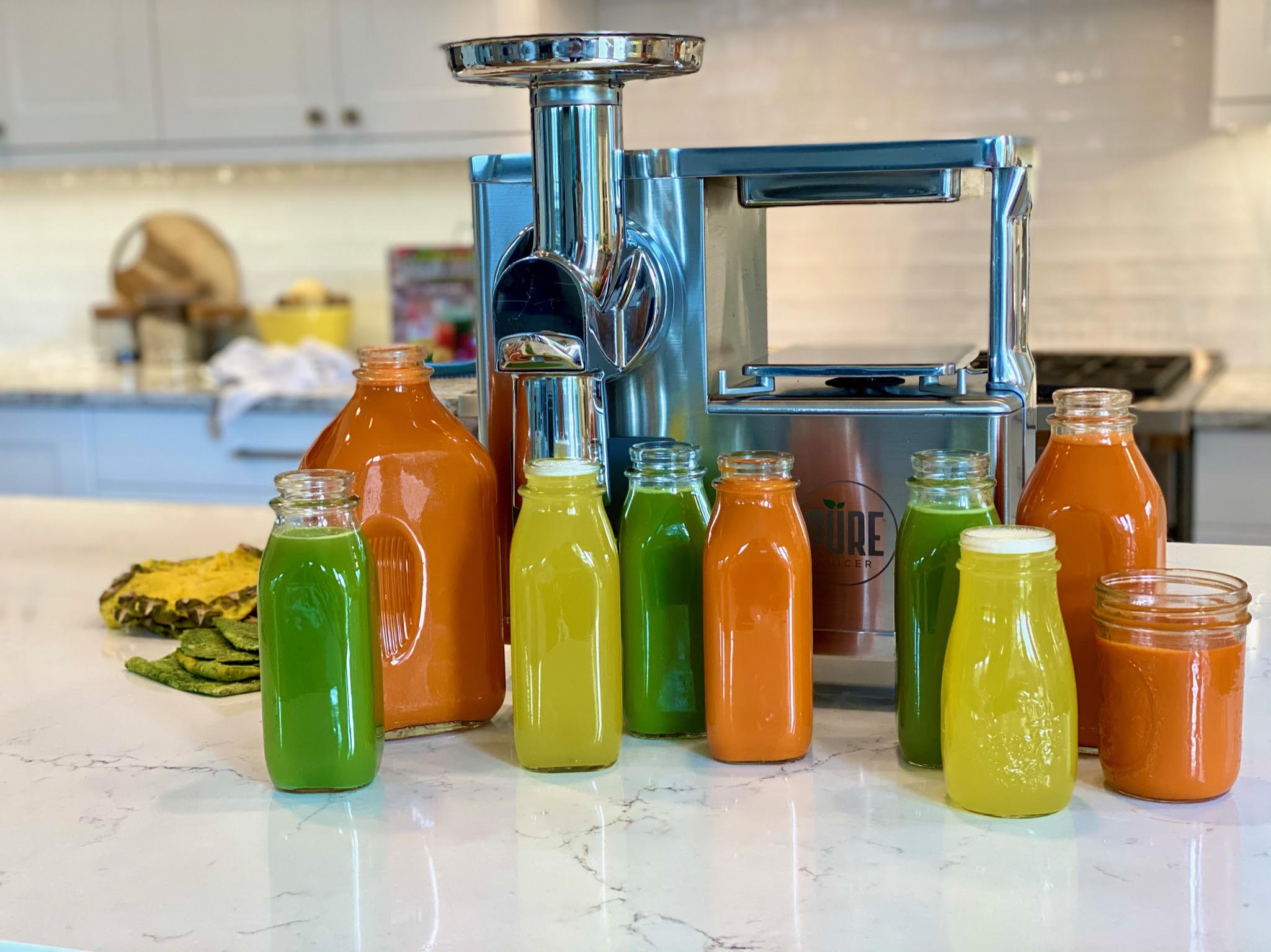 A line of glass bottles lined up in front of the PURE Juicer, in a rainbow